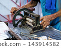 Close up hands of elderly man using a traditional vintage machine to press dried squid at a walking street food market in Thailand 143914582