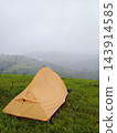 Freshness orange tent camping on green grass field on the mountain peak with mist and foggy in the morning of rain season of Thailand. Vertical photo 143914585