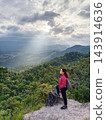 Smiling Asian woman with backpack travel wearing red sweater standing on the top of mountain peak and see view greenery forest for lonely with peaceful calm 143914636