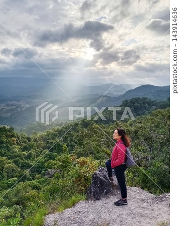 Smiling Asian woman with backpack travel wearing red sweater standing on the top of mountain peak and see view greenery forest for lonely with peaceful calm 143914636