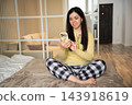 Young woman using a smartphone while sitting on a bed in a bedroom at night. Sleep hygiene screen time habits and digital wellbeing 143918619