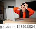 Stressed young woman holding her head while using laptop at home workspace. Digital wellbeing technology stress and online work overload 143918624