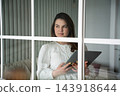 Woman holding tablet and smartphone behind glass partition in a modern home interior. Digital education self-paced online learning and mobile technology 143918644