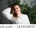 Woman lifting her hair at the roots while posing beside indoor green plants. Hair care volume styling and root lift 143918645