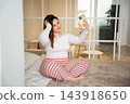 Young woman taking a self portrait with smartphone while sitting on bed in a bright home interior. Social media personal profile photo and online identity 143918650