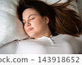 Woman resting with eyes closed on a white pillow in bed at home. Sleep quality comfortable bedding and restorative wellness 143918652