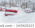 Red Car Buried Under Deep Snow. Heavy Winter Snowfall. Bright car remains buried under snow in parking lot, severe winter weather. Heavy snow covers car, transportation disruption, extreme cold 143920323