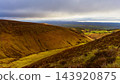 Widespread landscape view of green valley and brown hills under heavy grey clouds during daytime. 143920875