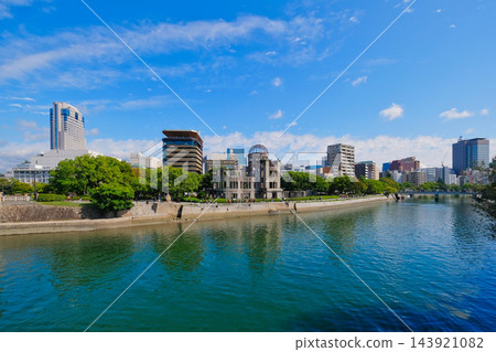 A view of the Atomic Bomb Dome and the city of Hiroshima against a blue sky, seen across the Motoyasu River. 143921082