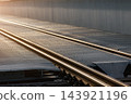 Closeup detail railway tracks on industrial steel bridge at sunset, with metal grating and glowing rails fading into distance. Evening sunlight highlights transport infrastructure and geometric lines 143921196