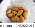 A batch of fresh russet potatoes nestled in a white paper bag, showing earthy skins and natural dirt. Ideal for recipes, farm produce imagery, grocery and culinary projects. 143922194