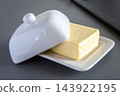 Domestic fresh block of butter in white ceramic box on the gray kitchen table. Baking or cooking ingredient. 143922195