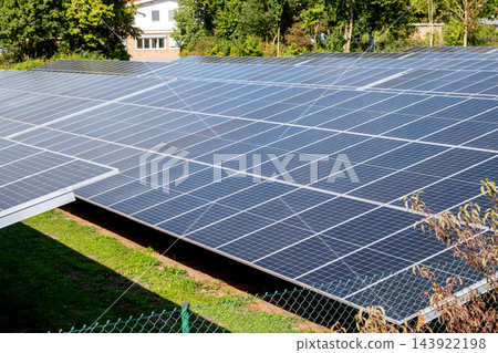 A large solar panel array framed by green shrubs near the house in the little city, illustrating renewable energy, sustainable power generation and clean technology in an outdoor solar farm setting un 143922198
