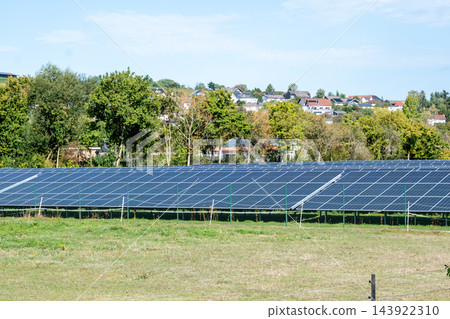 A large solar panel array framed by green shrubs near the houses in field, illustrating renewable energy, sustainable power generation and clean technology in an outdoor solar farm setting under natur 143922310
