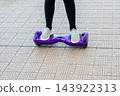 Girl in sneakers riding the violet hoverboard on the brick road. New technologies. Self balancing electric smart skateboard. Electrical scooter for play outside. 143922313