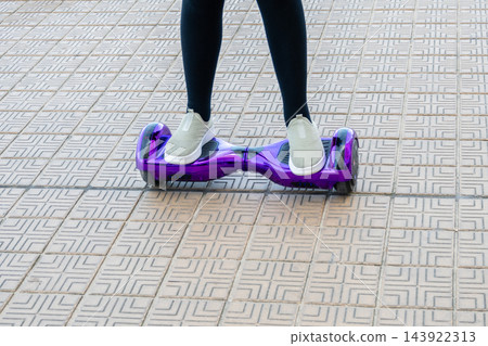 Girl in sneakers riding the violet hoverboard on the brick road. New technologies. Self balancing electric smart skateboard. Electrical scooter for play outside. 143922313