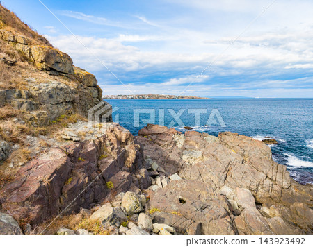 Rock shoreline beside blue water and distant land under a cloudy sky during daytime Rock shoreline beside blue water and distant land under a cloudy sky during daytime 143923492