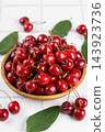 Fresh ripe sweet cherry in wooden bowl with green leaves on light background, healthy organic fruit 143923736