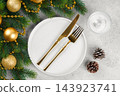 Elegant Christmas table setting with gold cutlery on white plate and decorated spruce branches 143923741