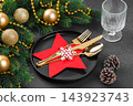 Festive Christmas table setting, dinnerware. Black plate and gold cutlery in red star shaped holder 143923743