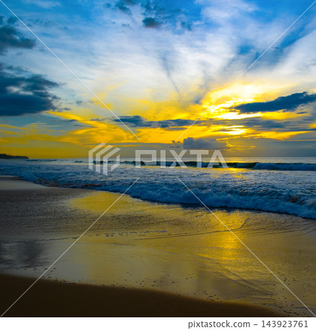 Dramatic sunset sky over tropical sea waves and wet sandy beach shoreline in square format with bright sun flare Dramatic sunset sky over tropical sea waves and wet sandy beach shoreline in square format with bright sun flare 143923761