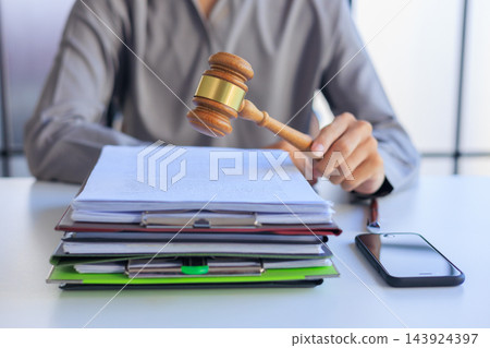 Attorney holding a wooden gavel above a pile of court paperwork on a workspace table. 143924397