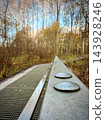 Metal footbridge with circular plates through a leafless woodland landscape 143928246