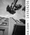 Monochrome upward view of modern building facade and trees beneath cloudy sky 143928256