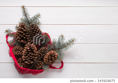 Mesh red cotton bag with Christmas fir tree branches on wooden board. Zero waste. Eco friendly Xmas. Mesh red cotton bag with Christmas fir tree branches on wooden board. Zero waste. Eco friendly Xmas. 143928675