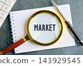A magnifying glass rests over the word market on a notebook with a pen and calculator on a desk 143929545