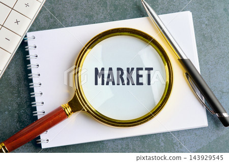 A magnifying glass rests over the word market on a notebook with a pen and calculator on a desk A magnifying glass rests over the word market on a notebook with a pen and calculator on a desk 143929545