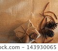 Eco-friendly gift box wrapped in craft paper with pine cones on rustic burlap background  143930065