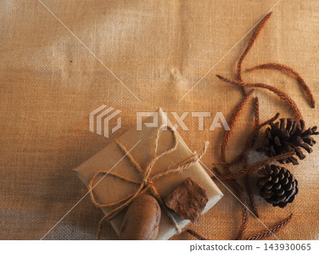 Eco-friendly gift box wrapped in craft paper with pine cones on rustic burlap background Eco-friendly gift box wrapped in craft paper with pine cones on rustic burlap background 143930065