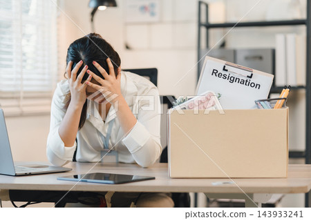 Frustrated office worker holding head beside packed box with resignation letter, conveying stress Frustrated office worker holding head beside packed box with resignation letter, conveying stress 143933241