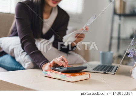 Close up of woman using calculator and holding receipts while managing finances at home. Close up of woman using calculator and holding receipts while managing finances at home. 143933394