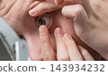 Person inserting a contact lens into an eye while looking into a mirror during close up personal care 143934232