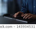A businessman using a computer at a desk in a darkened room. Close-up of his hands and keyboard. Technology in business. 143934531