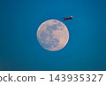 A telephoto shot capturing an ANA plane, glowing crimson in the sunset, ascending past the full moon at dusk in winter from Honmoku Pier. A telephoto shot capturing an ANA plane, glowing crimson in the sunset, ascending past the full moon at dusk in winter from Honmoku Pier. 143935327