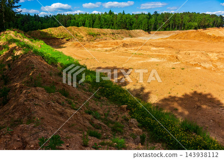 Scarred landscape of an open-pit sand quarry with massive earth mounds and piles of soil, cutting deep into the green forest line, dramatic evidence of industrial land transformation Scarred landscape of an open-pit sand quarry with massive earth mounds and piles of soil, cutting deep into the green forest line, dramatic evidence of industrial land transformation 143938112