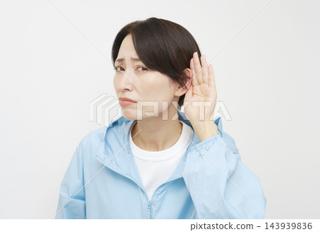 一位身材健美的中年女性，在白色背景下，用手摀著耳朵認真聆聽。 143939836