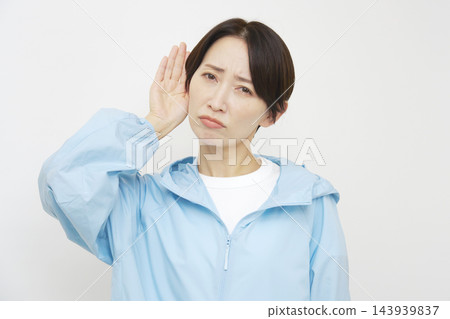 一位身材健美的中年女性，在白色背景下，用手摀著耳朵認真聆聽。 143939837