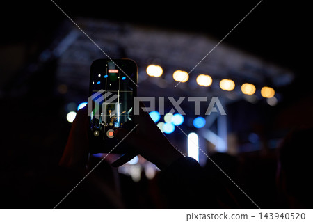 Person recording live concert on smartphone at night 143940520