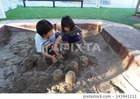 兩個男孩在公園的沙坑玩耍，堆沙堡。 143941211