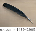A beautiful, glossy black bird feather placed on a simple wooden table. 143941905