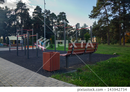 Empty wooden bench and pull up bars on modern calisthenics sports ground surrounded by green trees in public park outdoors Empty wooden bench and pull up bars on modern calisthenics sports ground surrounded by green trees in public park outdoors 143942734