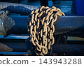 Rusty Iron Chain Wrapped Tightly Around Industrial Metal Pipe at Maritime Port Facility 143943288