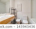 Modern bright bathroom with wooden countertop sink, white toilet, bidet, and built-in bathtub in light tiled interior with clean minimalist residential styling, with bathroom, modern, bright, wooden 143943436