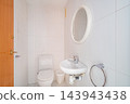 Clean modern white bathroom with toilet, compact wall-mounted sink, round mirror, chrome faucet, and bright tiled walls in minimalist residential interior, with bathroom, toilet, sink, mirror detail 143943438