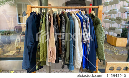 Assorted second hand jackets, coats and shirts hanging on wooden clothing rack at outdoor vintage clothing market 143943940