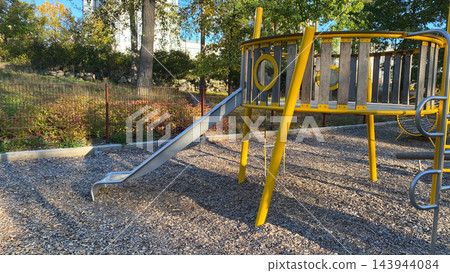Empty outdoor playground with metal slide and yellow climbing structure on wood chip surface on sunny autumn day Empty outdoor playground with metal slide and yellow climbing structure on wood chip surface on sunny autumn day 143944084